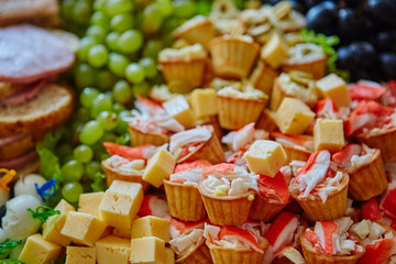 Lots of snacks piled on a large plate. Crabs, cheese, tartlets, grapes, sausage, ham