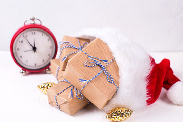 Obraz na płótnie Canvas Wrapped boxes with presents, decorative golden pine cones in Santa hat and vintage alarm clock on white textured background.