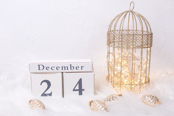 Calendar, fairy lights in decorative cage, decorative golden pine cones  on white fur background.