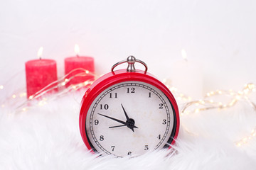 Red clock - symbol of  New Year and birning candles  on white fur background.