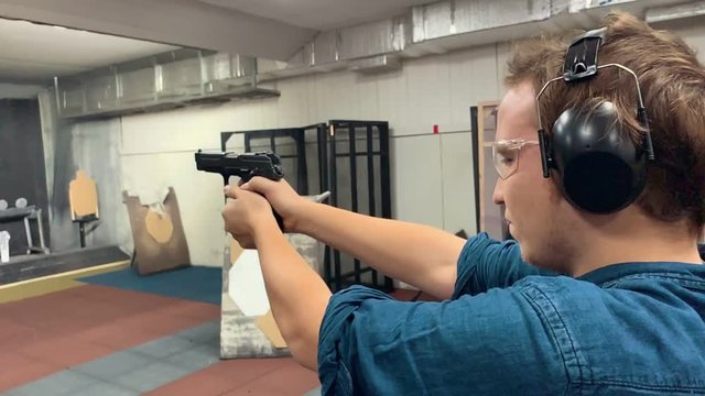 Young man aims, holding a gun at a shooting gallery, shooting range. Slow motion