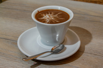 White cup of coffee on wooden table with spoon