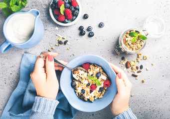 Healthy food background with homemade oatmeal granola or muesli with yogurt and fresh berries for healthy morning breakfast, top view, copy space. Women's hands