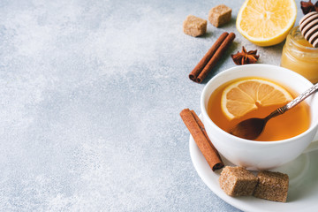 Cup of tea with lemon and brown sugar, cinnamon and anise on the table.