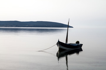Fishing boat anchored in a sea bay with flat water that merges with the white sky