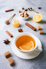 Cup of tea with lemon and brown sugar, cinnamon and anise on the table.