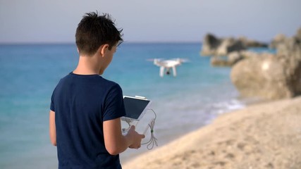 Young boy operating a flying drone on a coast of a sea. - Powered by Adobe