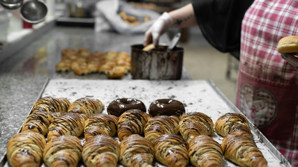 Bäckerin glasiert Donuts und Croissants mit Schokolade in Backstube - Variante 2