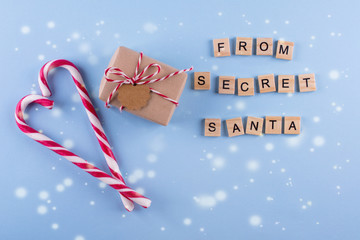 Present from secret Santa. Wrapped gift box with notes,  candy cane on blue pastel background. Top...