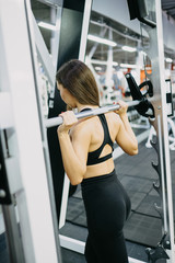 Fototapeta na wymiar beautiful fitness young girls doing squats with the barbell in smith machine at the gym. Perfect fitness female figure