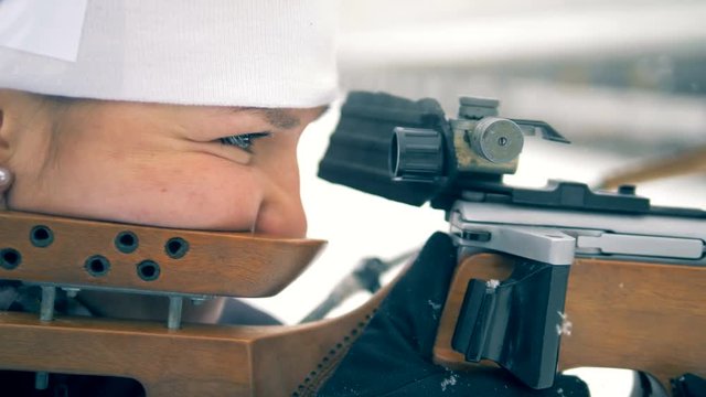 Side view of a lady athlete aiming from biathlon weapon