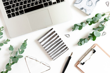 Workspace with laptop, notebooks, calligraphy pen, eucalyptus branches, clipboard, glasses on a white background