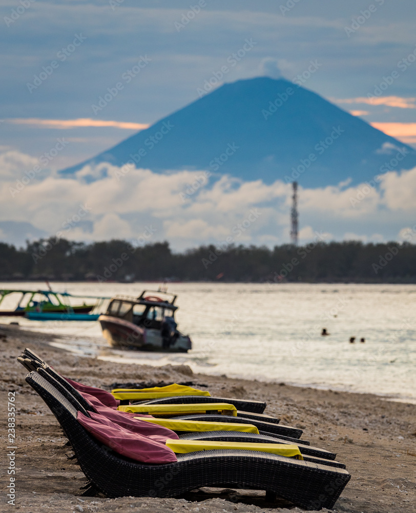 Wall mural Empty beach loungers on the sand with a volcano and fishing boats in the background