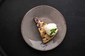 Slice of Blueberry Pie with vanilla ice cream on grey plate on black background