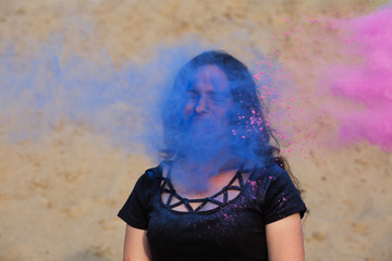 Lovely young woman posing with exploding around her blue and purple Holi powder at the desert