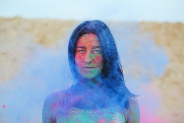 Closeup shot of a lovely tanned young woman having fun in a cloud of blue dry Holi paint