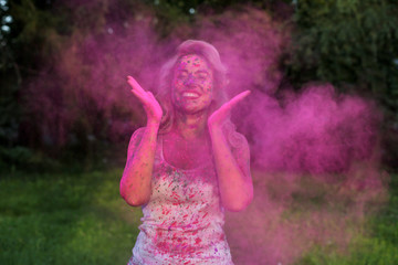 Portrait of positive young model having fun with a cloud of pink dry Holi paint at the park