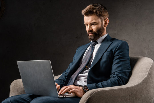 successful businessman sitting in armchair and typing on laptop