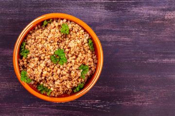 Buckwheat in a rustic earthenware bowl, garnished with fresh parsley leaves, shot from the top on a dark wooden background with a place for text
