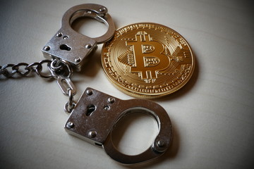 An golden Bitcoin, an virtual currency in physical coin form, displayed with handcuffs, symbolic...
