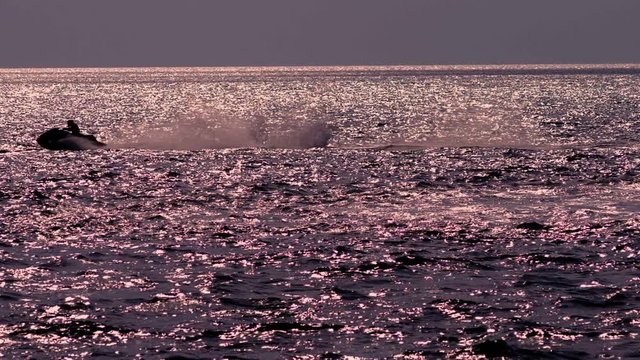 silhouette, a men on a motorbike floats on the sea.