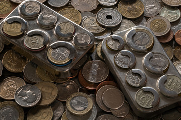 Metal coin boxes lie on a pile of various coins.