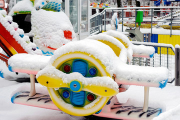 The first snow covered the children's carousel in the form of an airplane in the park. Children's...
