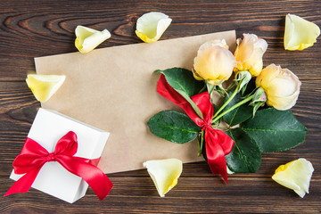 Yellow roses with red bow and greeting card on wooden background. Women's day. Valentines day. Birthday.