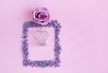 Flowers in a frame and a glass bottle of perfume on a pink background. Place for text.