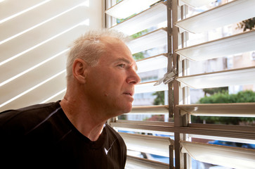 man stares out the window through the blinds