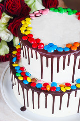 White Birthday cake with colorful Sprinkles over a light background with a bouquet of roses
