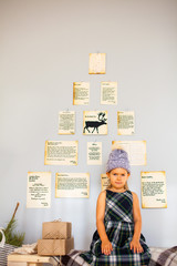 Little funny girl sitting near grey Chistmas wall