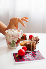 A cup with cacao and marshmallow and childs hand, side view