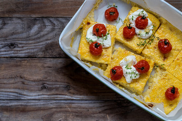 polenta with baked tomatoes and cream cheese, thyme on wooden background