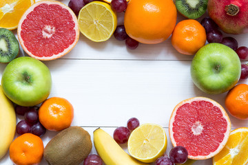 Fruit frame background with oranges, tangerines, banana, apple, lemon on white wooden table, healthy food frame