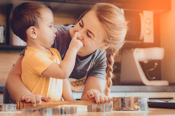Obraz na płótnie Canvas happy funny blonde mother and child baby boy bake christmas cookies. Concept of family leisure in the kitchen, the child is preparing food various dishes: pasta, cookies, bread, gingerbreads.