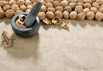 Large group of wallnut, pestle and mortar over jute background with space for your text. 
