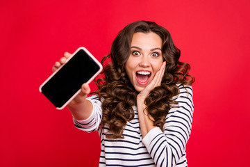 Close-up portrait of nice crazy funny attractive amazed stunned wavy-haired lady wearing striped pullover showing black screen display gadget device isolated over bright vivid shine red background
