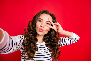 Fototapeta premium Self-portrait of nice cute lovely sweet pretty attractive positive cheerful wavy-haired lady wearing striped pullover showing v-sign near eye isolated over bright vivid shine red background