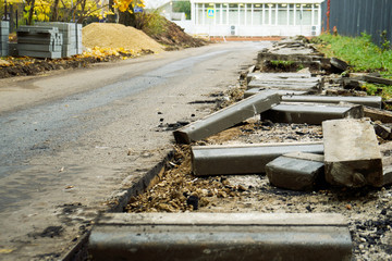 Road curb replacement on the Moscow street in Autumn. Broken freshly dug up old curbstones with pieces of an asphalt and earth lying on the road.