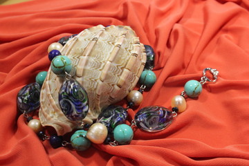 Large sea shell and necklace of semi-precious natural stones - lapis lazuli, turquoise, pearls and glass beads on a pink background.