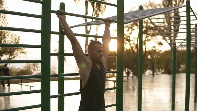 Strong fit man workout out on horizontal bars outdoors . Young man training abnominal muscules lifting legs high to the head doing push ups outdoors during the morning sunrise
