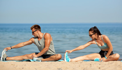 Fototapeta na wymiar fitness, sport and lifestyle concept - happy couple stretching legs on beach before training