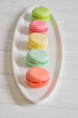 Close up. Colorful french macarons lined up in a row on white plate. Pastel colors.