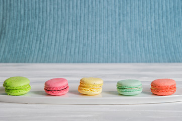 Close up. An assortment of bright colorful macaroons lined up in a row on a wooden white table. Blue knitted background. Copy space.
