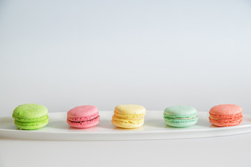 Close up. An assortment of bright colorful macaroons lined up in a row on a white plate. White background. Copy space.