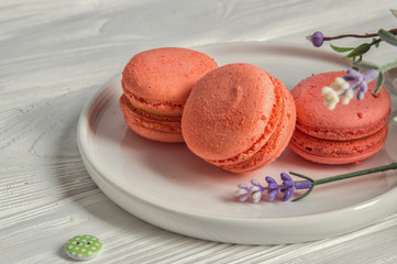 Close up. Color living coral. Bright macarons with mango, a vintage button, a lavender. White wooden background.