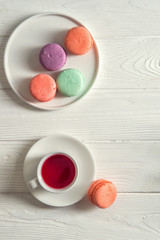 Top view. Close up. Provence breakfast. Bright macarons on a round plate, a cup of berry tea, a rustic white background. Vertical position. Copy space.
