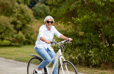 Naklejka premium active old age, people and lifestyle concept - happy senior woman riding fixie bicycle at summer park