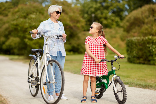 family, leisure and people concept - happy grandmother and granddaughter with bicycles at summer park